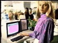 Grainy footage of a woman in a nineties department store typing at a beige computer terminal.