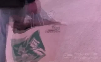 Archival footage of shoppers carrying bags through a nineties shopping mall.